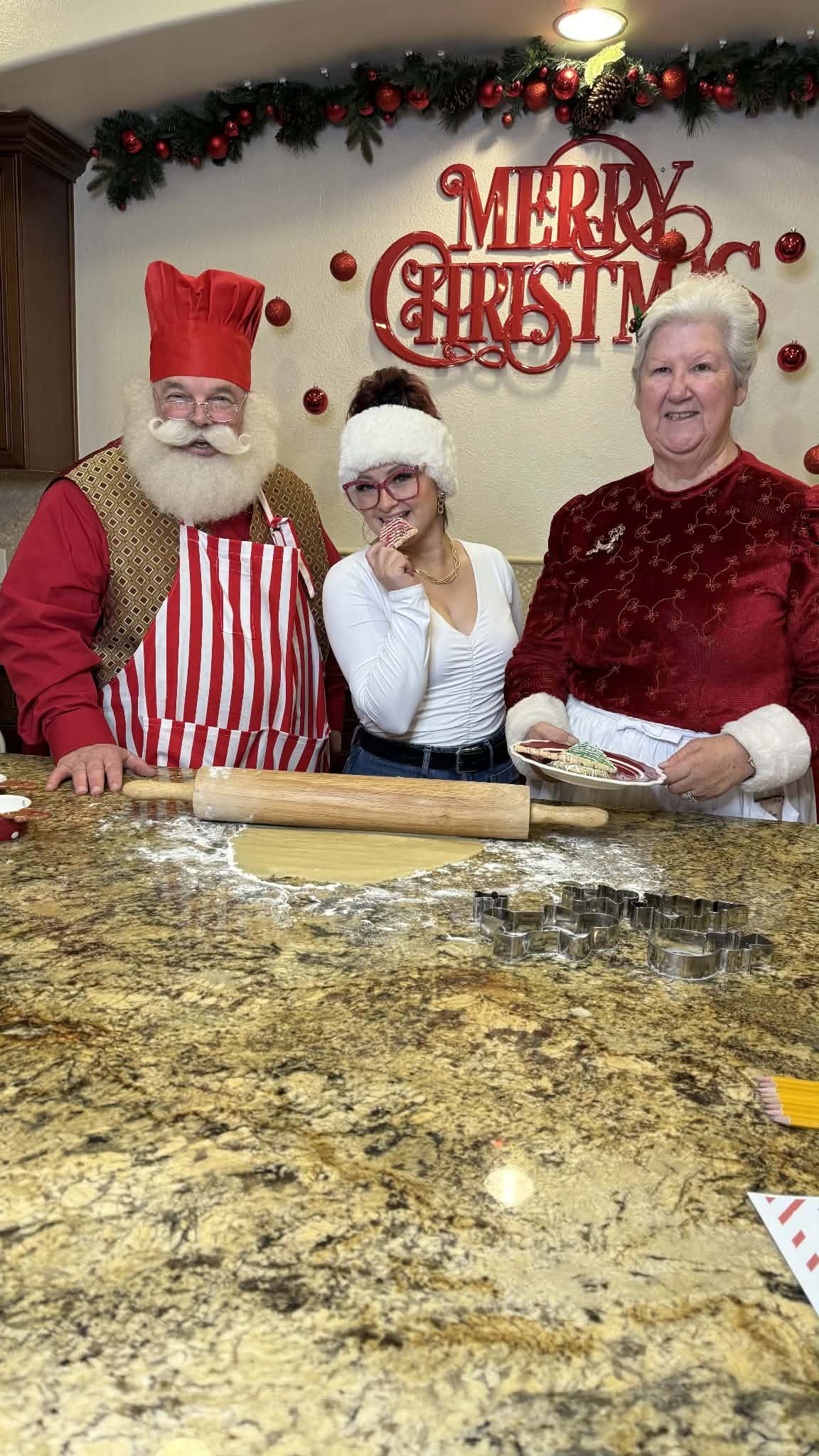 Santa and Mrs. Claus baking cookies with a teenager who is tasting the frosting