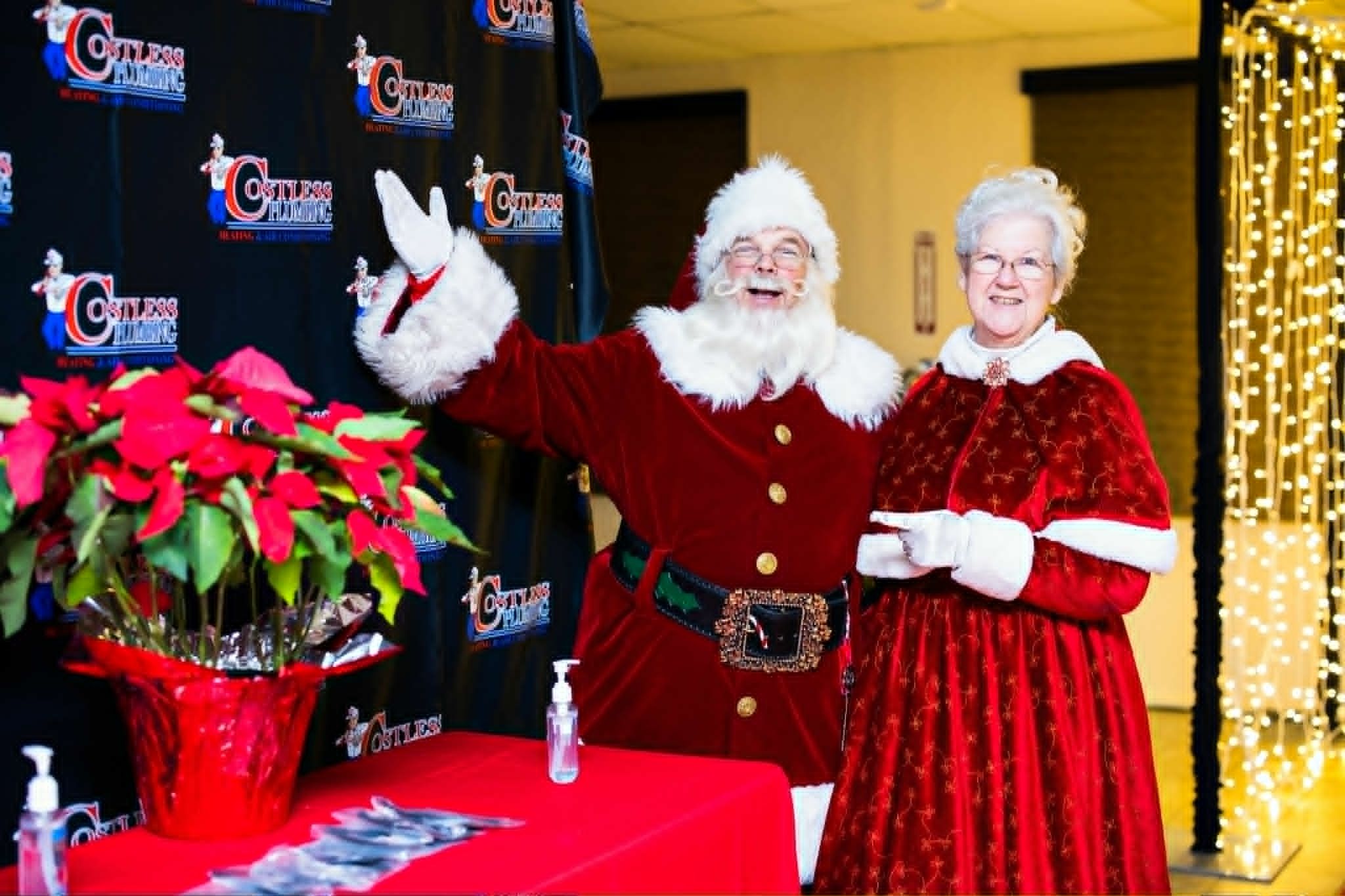 Santa waving and Mrs. Claus smiling at a company holiday event in front of a branded backdrop