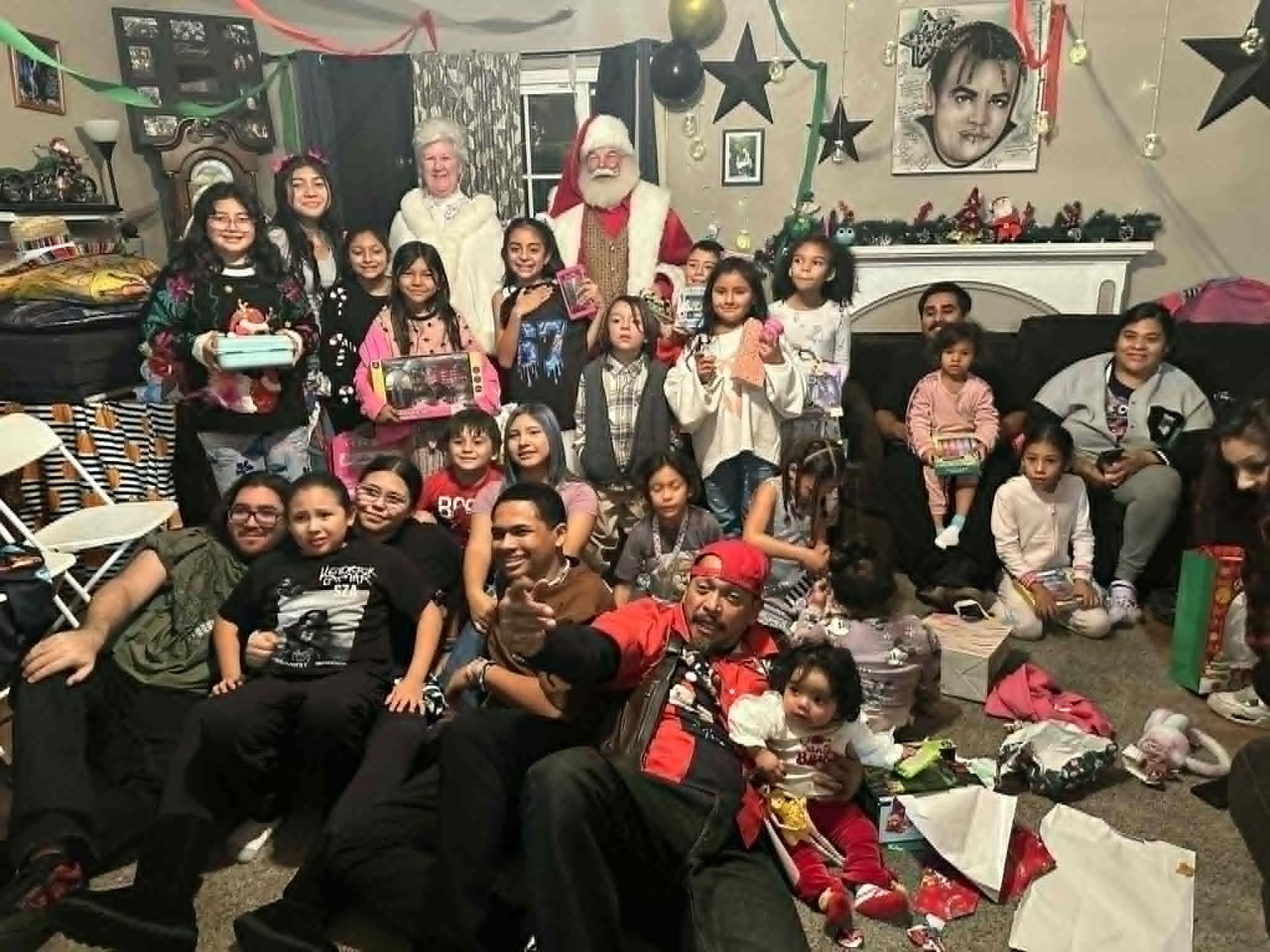 Santa and Mrs. Claus with a large extended family in a living room, children holding wrapped gifts